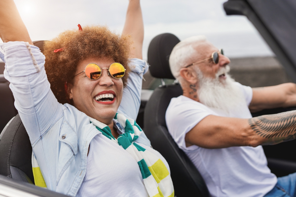 Senior interracial hipster couple driving their new convertible and celebrating.