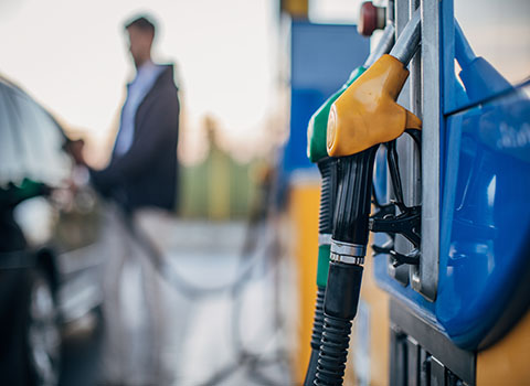 Close up of gas pump with a man filling up his car in the background